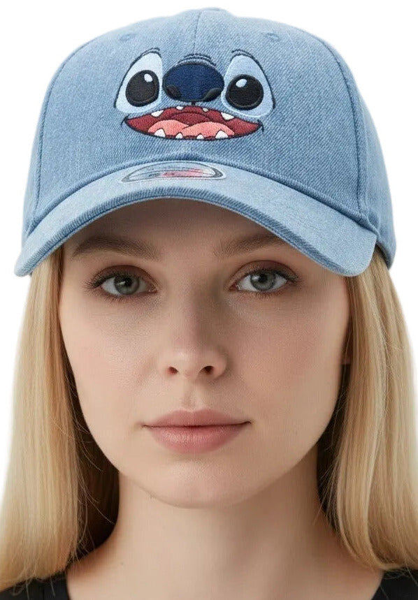 A woman wearing a light blue denim baseball cap featuring a stitched character face on the front, photographed against a plain light gray background.