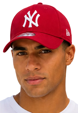 A close-up of a man wearing a red New York Yankees baseball cap with a white embroidered NY logo on the front and a white New Era flag on the side, set against a light blue sky background.