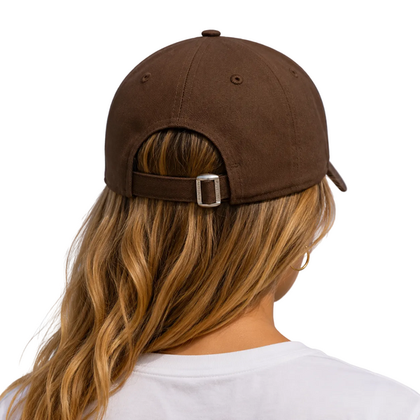 A person viewed from behind wearing a brown baseball cap with an adjustable strap and silver buckle, photographed outdoors against a blue sky.
