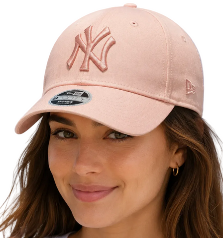 A woman wearing a light pink New York Yankees baseball cap with a matching embroidered 'NY' logo on the front and a New Era 9FORTY sticker on the brim, set against a plain white background.