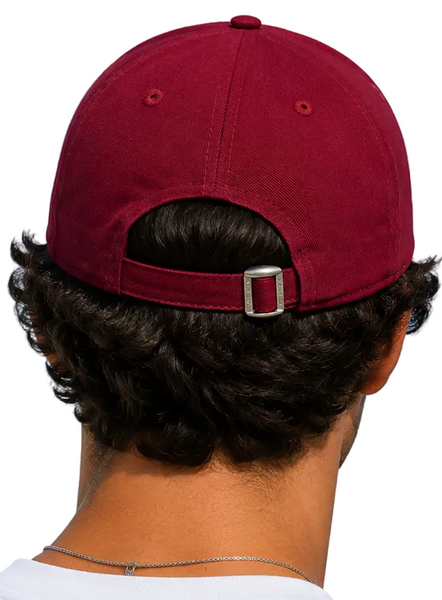 Two people shown from behind wearing matching burgundy baseball caps with adjustable straps and silver buckles, set against a solid light blue background.