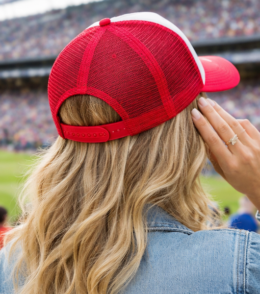 Woman wearing a red and white baseball cap with a stadium in the background rear